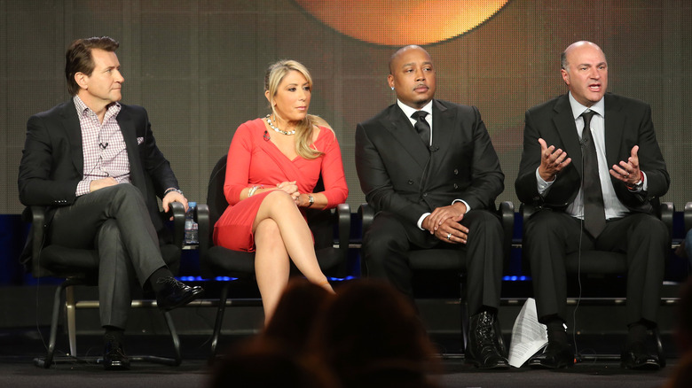 Robert Herjavec, Lori Greiner, Daymond John, and Kevin O'Leary sit on a panel at a conference.