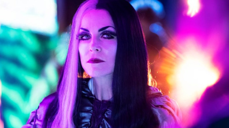 Lily Munster looks stern surrounded by colorful lights