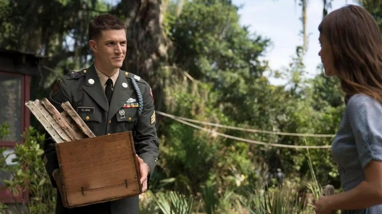 Jodie stands in military uniform holding wooden box of paintings