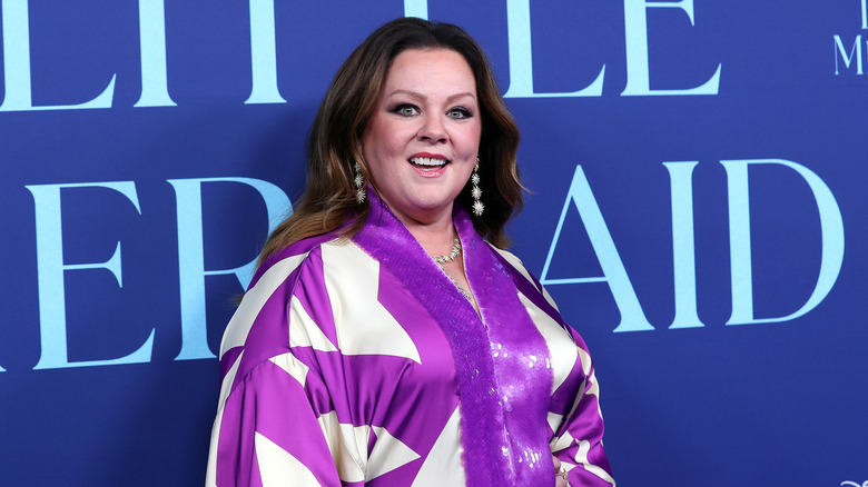 Melissa McCarthy smiling on red carpet, wearing white and purple outfit