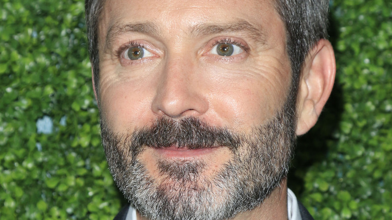 Thomas Lennon smiling beside a bush