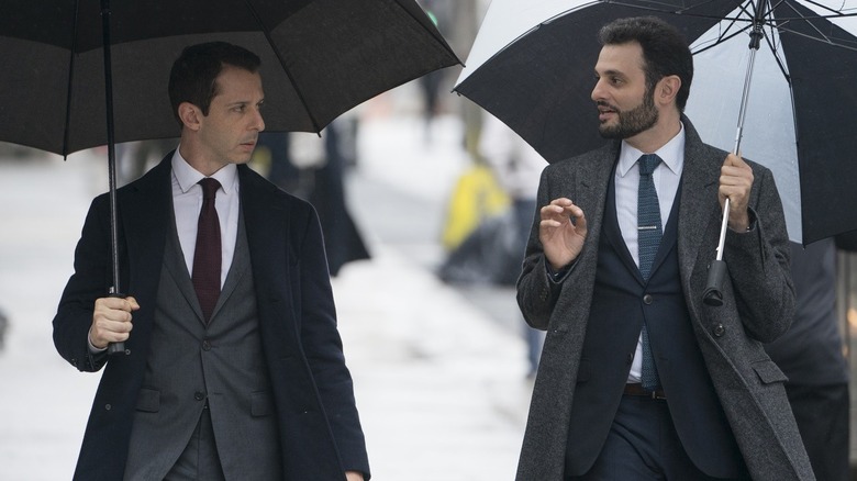 Arian Moayed and Jeremey Strong walking in suits with Umbrellas on Succession 