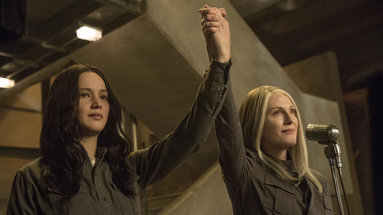 Katniss and Coin holding hands in a victorious post in The Hunger Games: Mockingjay