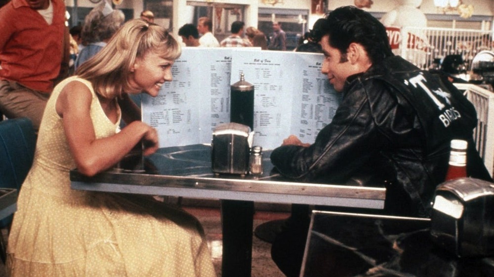 Sandy Olsson and Danny Zuko hiding behind menus at the diner in Grease