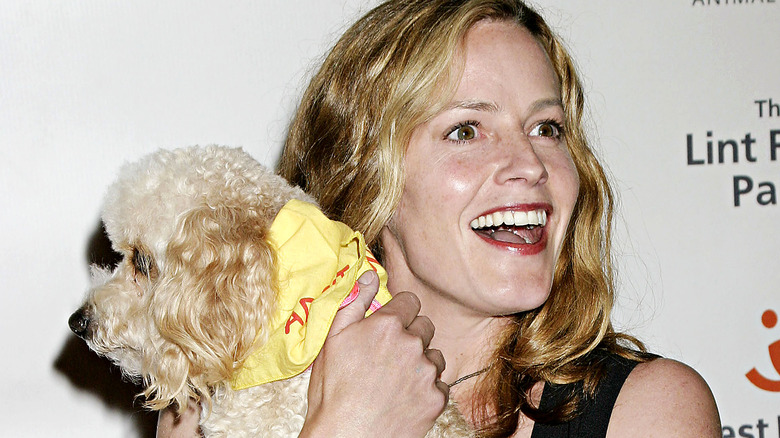 Elisabeth Shue carrying a dog and smiling