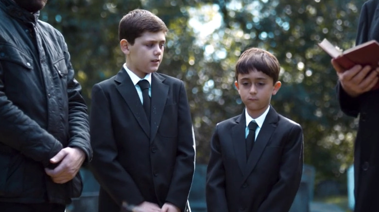 Young Liam standing at funeral with brother