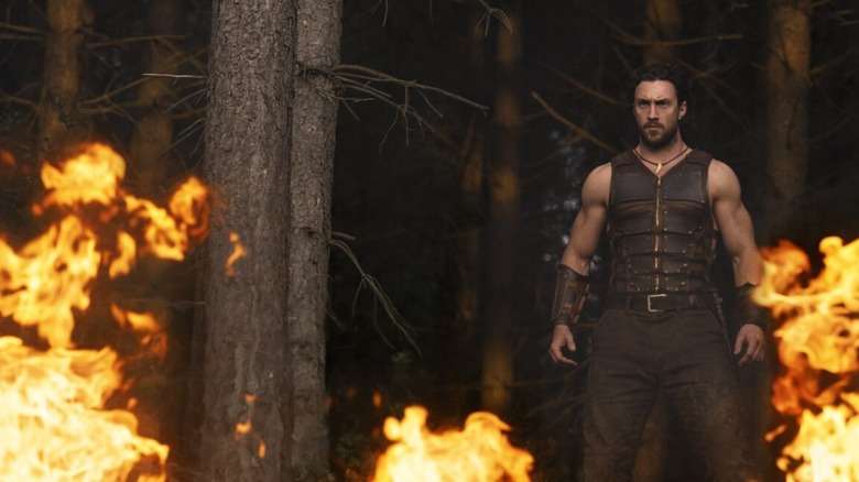 Kraven standing behind patches of fires in the woods