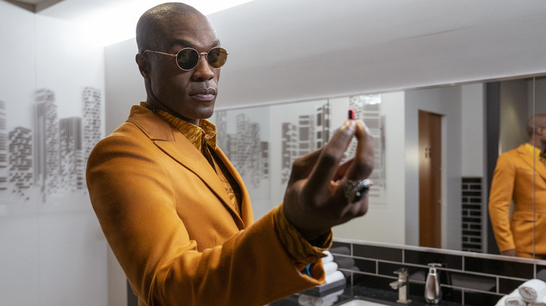 Morpheus in a golden yellow suit, holding up a red pill.