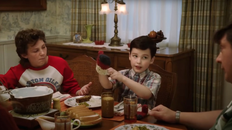 Young Sheldon putting on gloves during dinner 