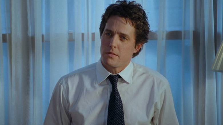 Hugh Grant stands near curtained window