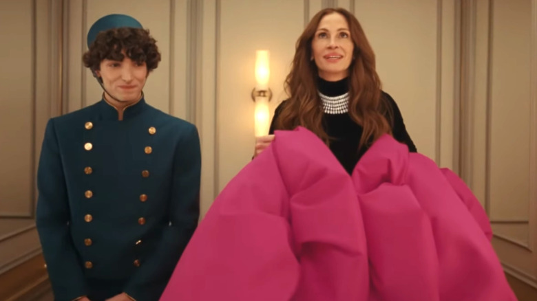 Julia Roberts stands in a black and pink ball gown next to a bellhop in an elevator