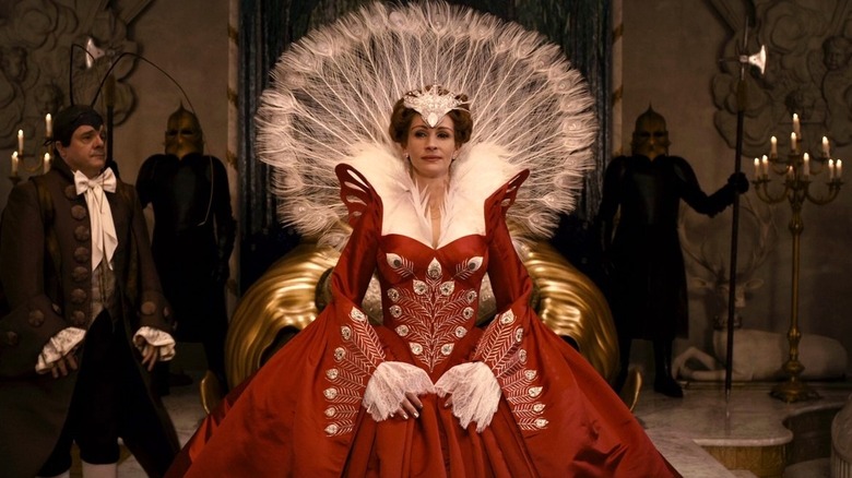 The Queen stands in front of a throne in a red ball gown with white feathers as Brighton walks behind her