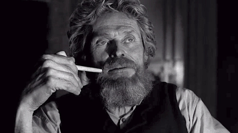 Willem Dafoe sits with a pipe