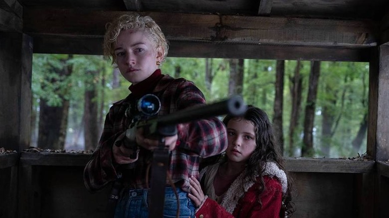 Charlotte aims a gun while Ginger clings to her in a shed in "Wolf Man" (2025)