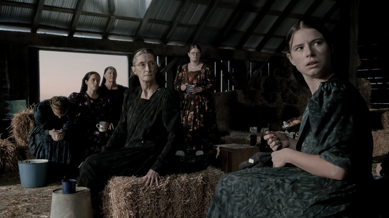 Six women in a barn look intently to the side