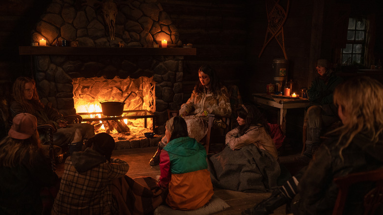 A group of teen girls huddles around a fireplace