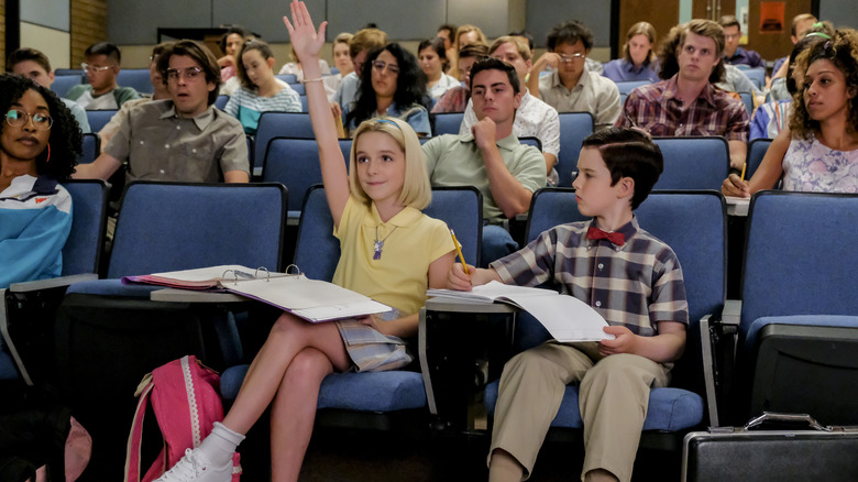 Paige raising her hand sitting next to Sheldon